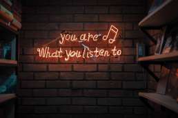 Red neon lights that form the words 'you are what you listen to'