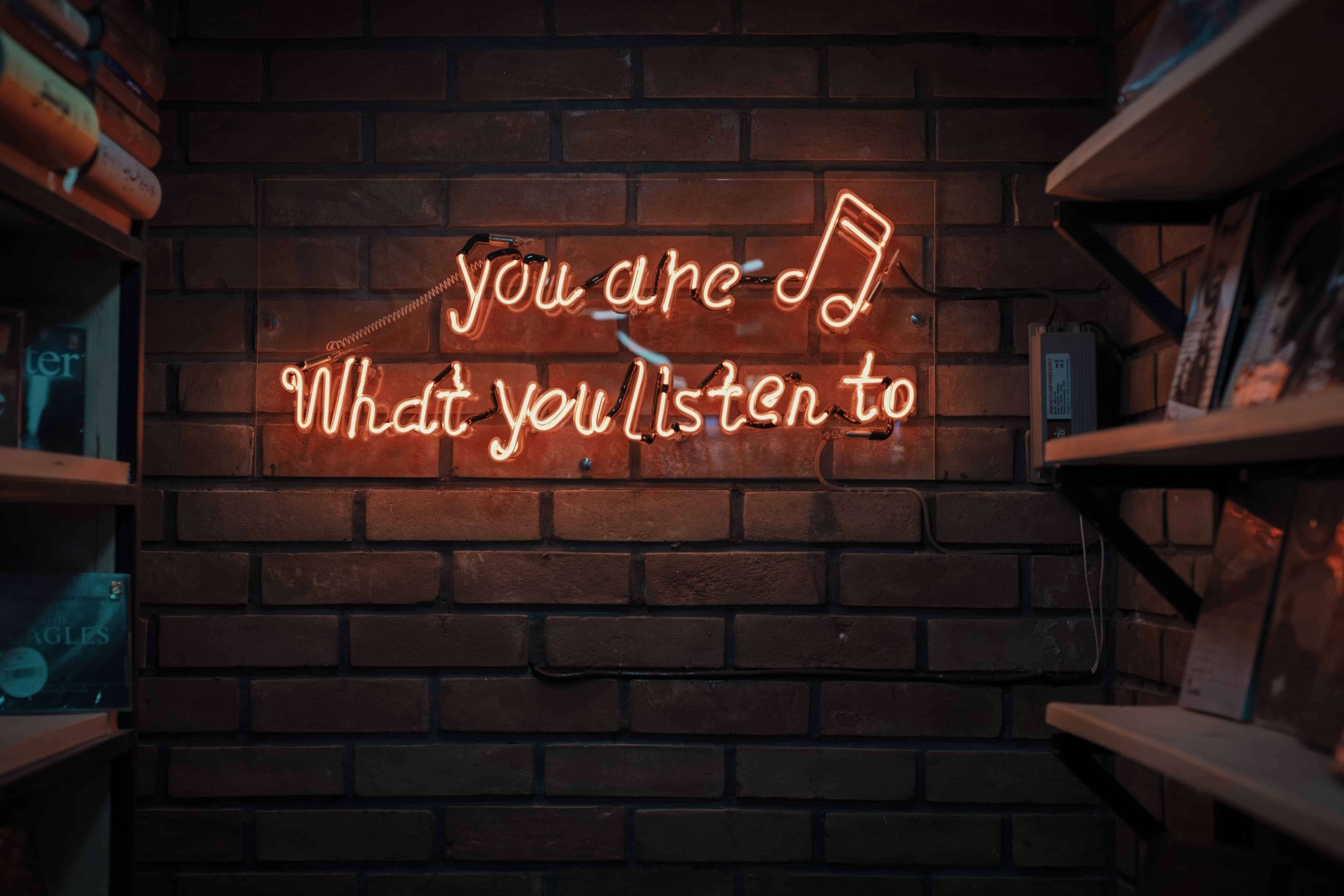 Red neon lights that form the words 'you are what you listen to'