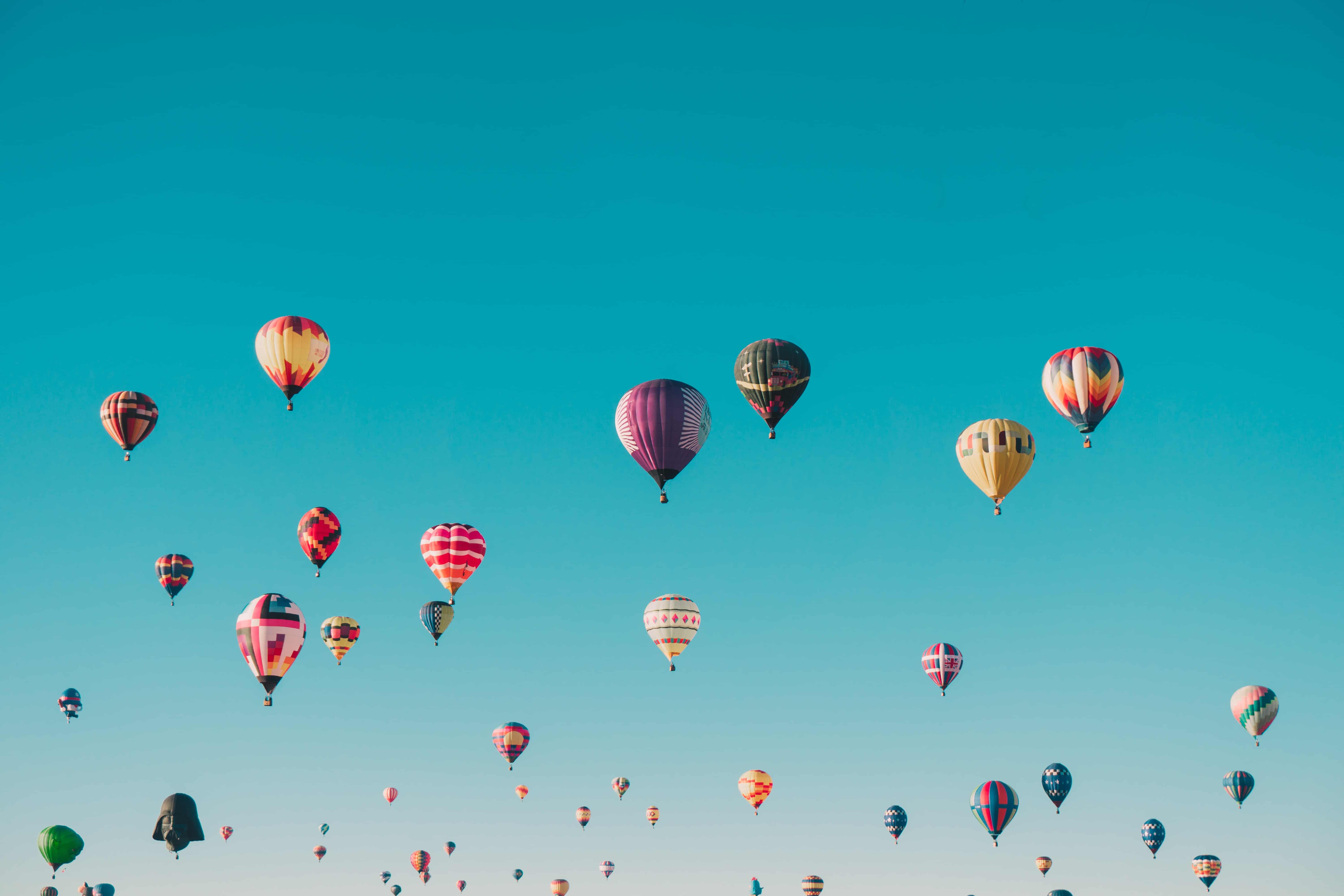 Multi-colored hot air balloons flying in clear blue sky