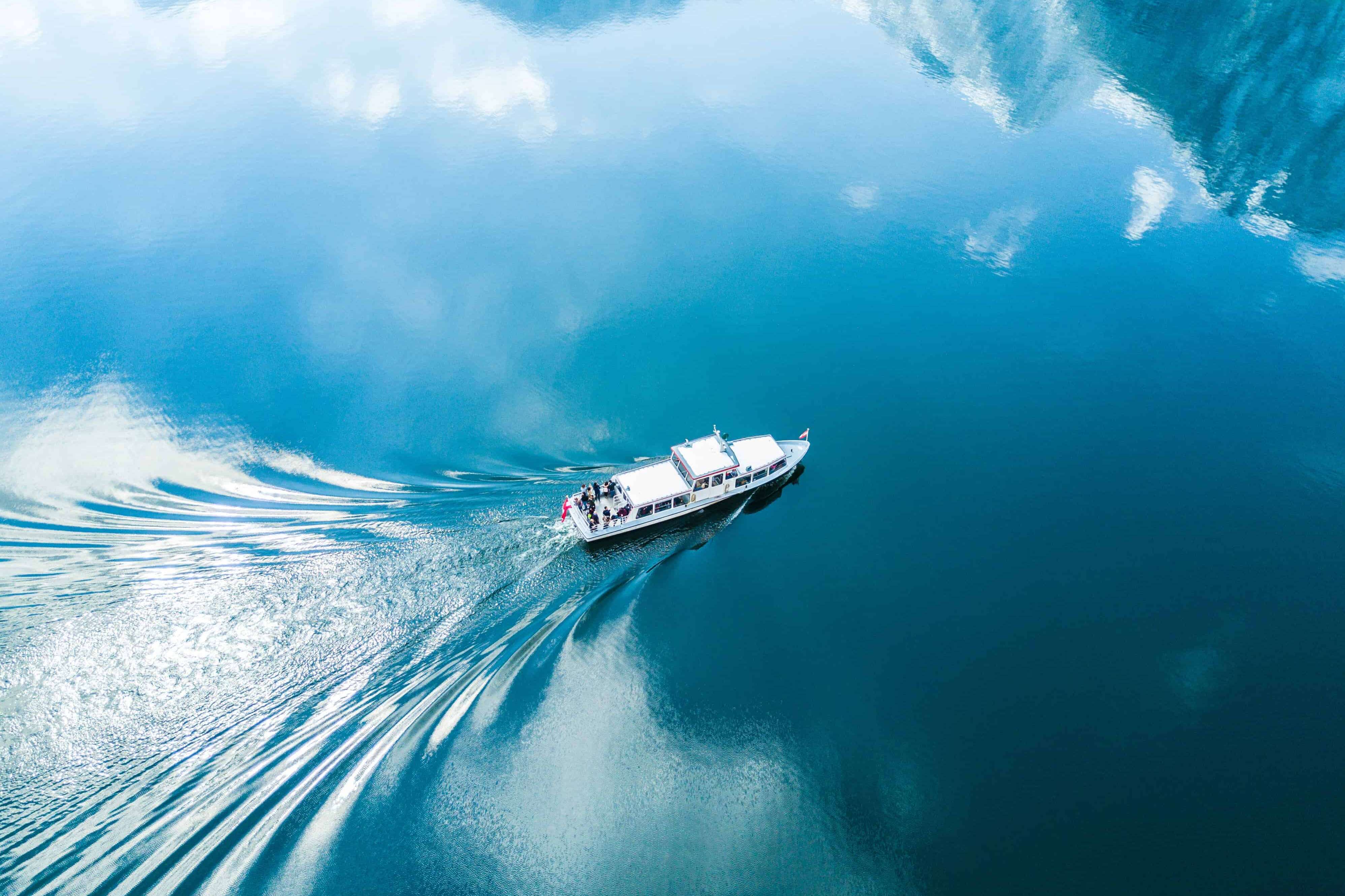 Boat sailing on blue water reflecting mountains