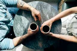 Two people sitting across from one another, holding coffee cups