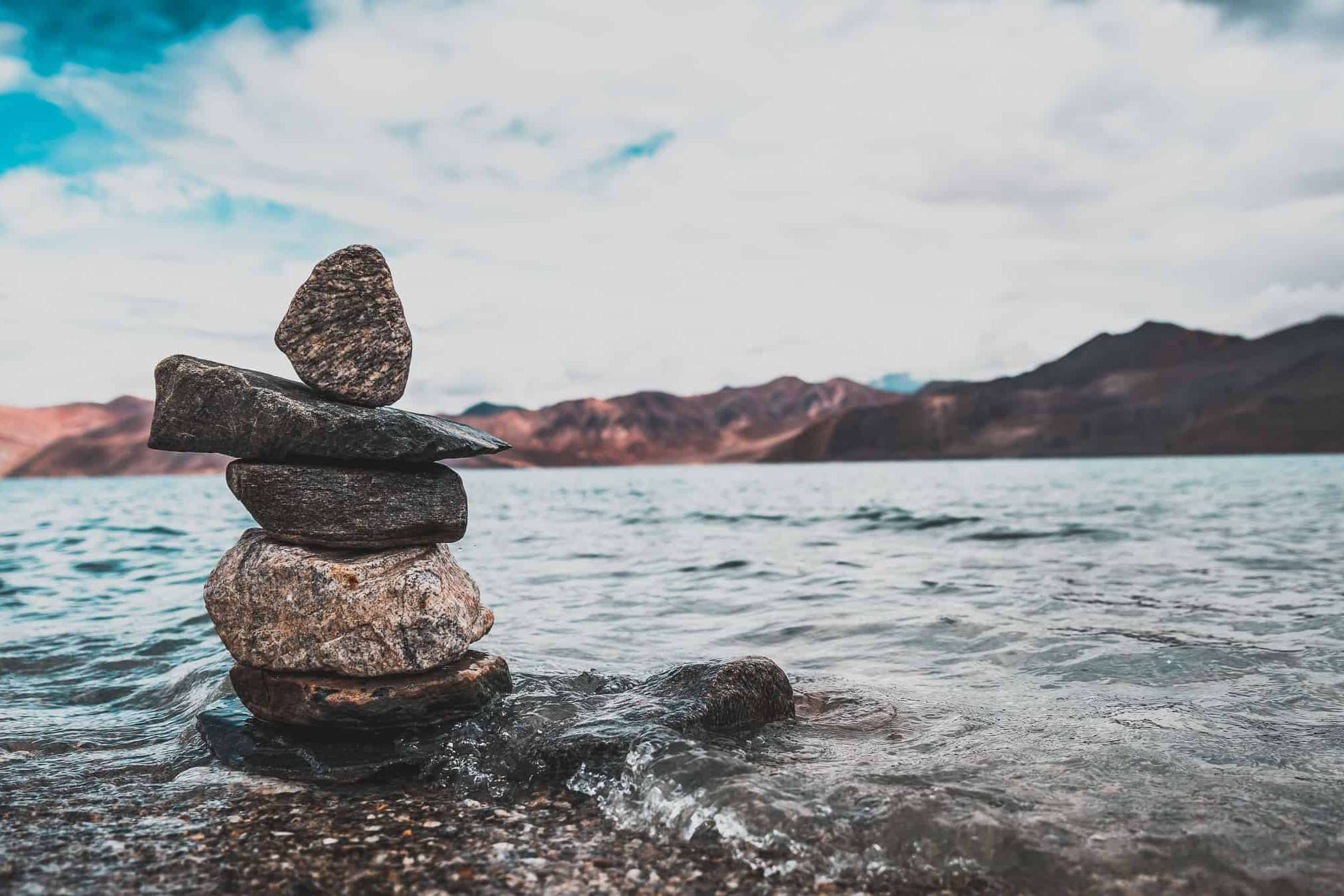 Rocks stacked in river with mountains and cloudy sky in background