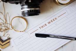 Empty weekly calendar, a pen, and a camera