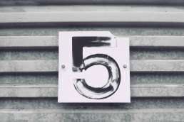 Number 5 painted on sign against metal wall