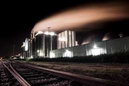 Photo of factory at night with lights on taken from rail road tracks