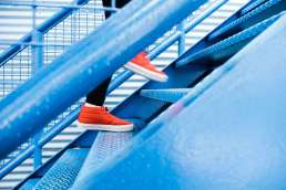 Person in red shoes and black leggings climbing blue stairs