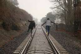 Two people walking on rail road tracks surrounded by trees and fog