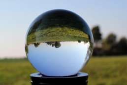 Crystal ball on post outside with inverted sky and ground in ball, and blurry sky and ground in background