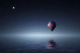 Hot air balloon floating low over a lake at night with moon in the background