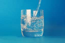 Water glass being filled with blue background