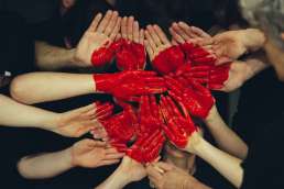 People with red painted hands holding their hands together to form a painted heart