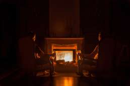 Two people sitting in armchairs in front of a lit fireplace