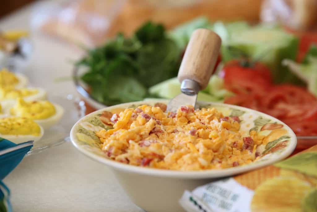 Bowl of Mac and Cheese with bacon bits with other picnic foods in the background