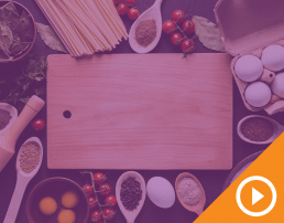 Cutting board surrounded by ingredients behind purple transparency with white play button on an orange triangle in the bottom right corner