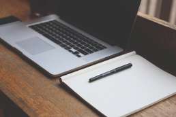 Blank laptop and notebook with pen sitting on wooden desk