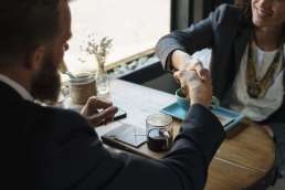 Man and woman shaking hands across a table and coffee