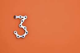 Number three made of linked bike chain on orange background