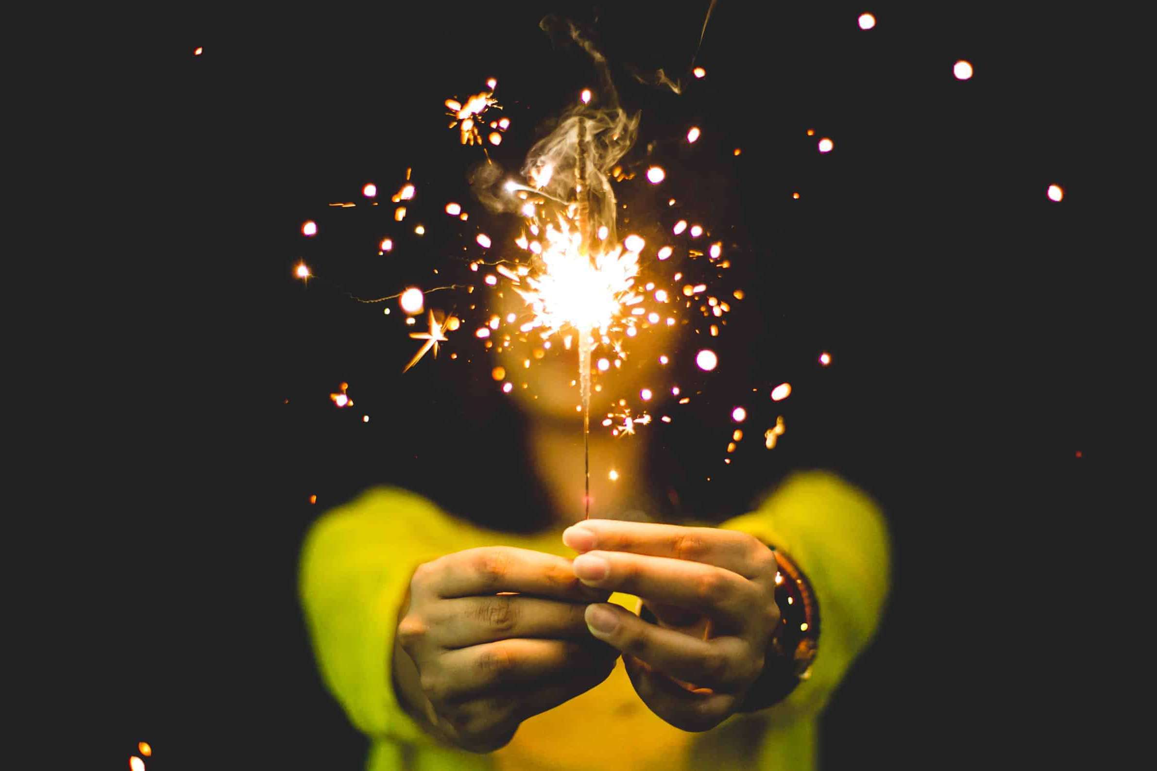 Woman in yellow sweater holding sparkler with black background