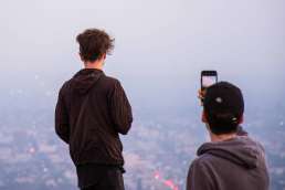 Two men overlooking city through fog and taking photos with cellphones