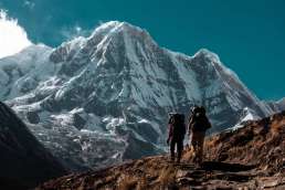 Two people hiking towards mountain with snow and blue sky