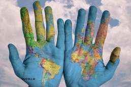 Hands with colorful world map painted on them held up in front of cloudy sky