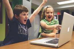 Young boy cheering and girl excitedly pointing at computer screen
