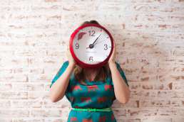 Woman holding a red clock over her face