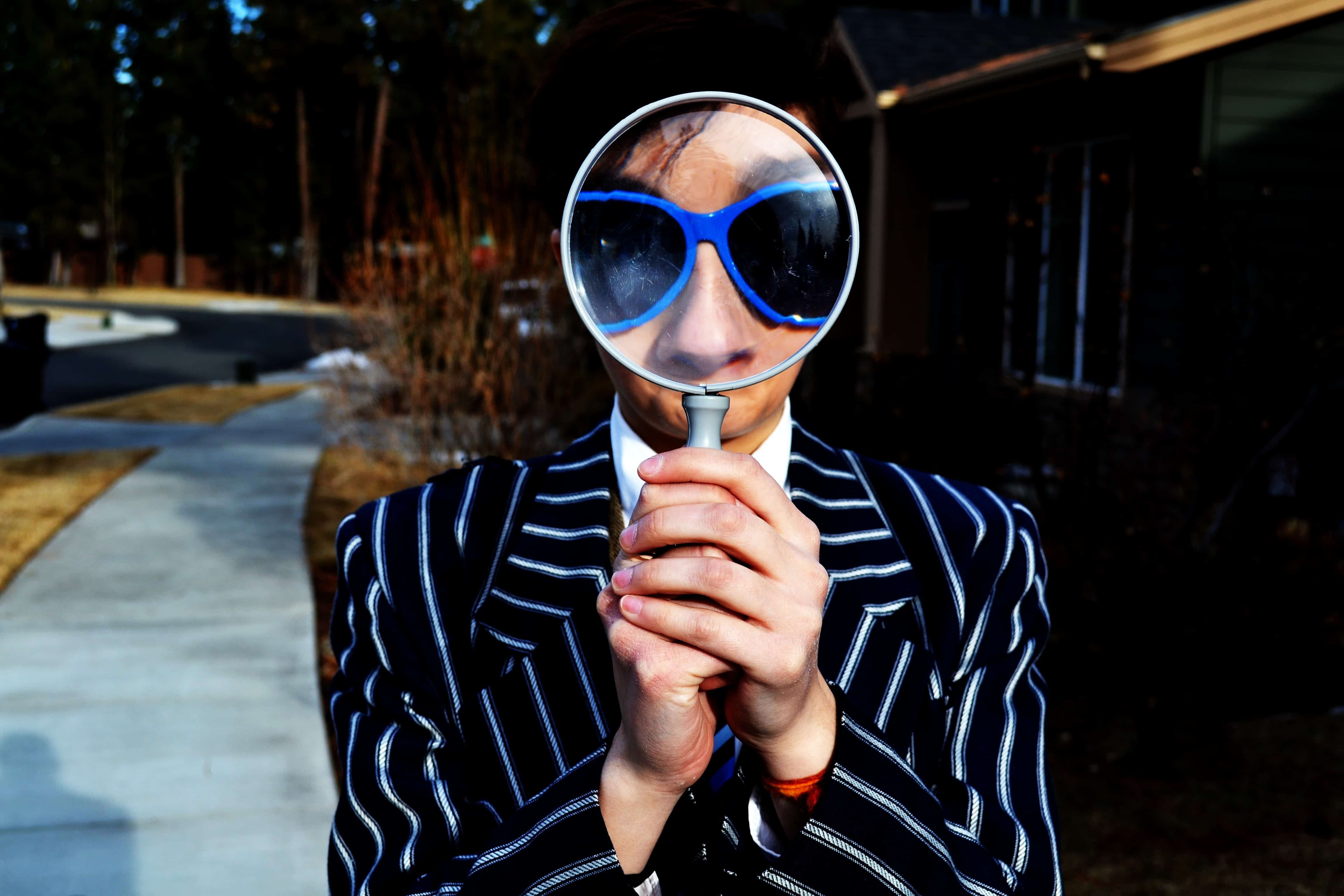 Person in sunglasses holding magnifying glass
