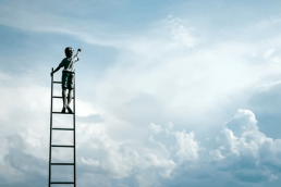 Boy on ladder reaching into cloudy sky
